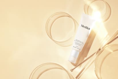 A skincare tube with clear glass bowls and soft lighting.