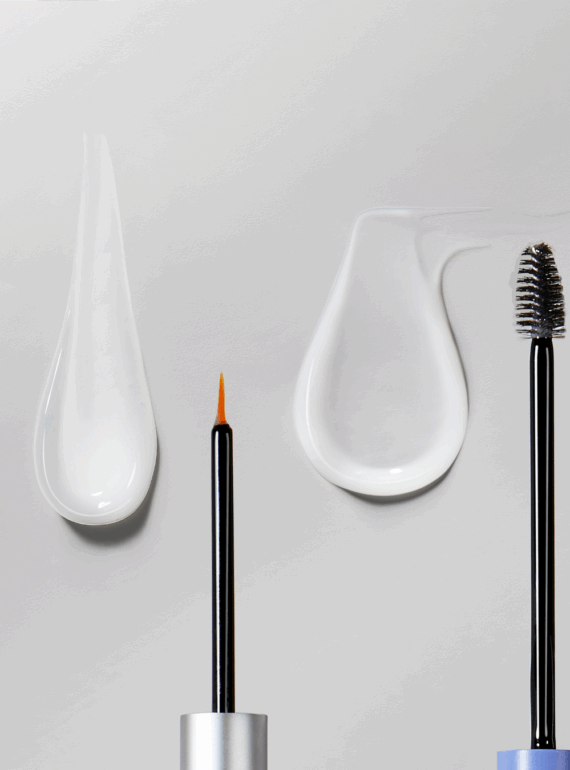 Two makeup brushes with foundation and mascara smears on a grey surface.