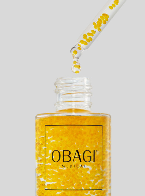 A dropper releasing golden serum from an Obagi bottle.