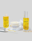 Three skincare products with yellow liquid and cream on a white surface.